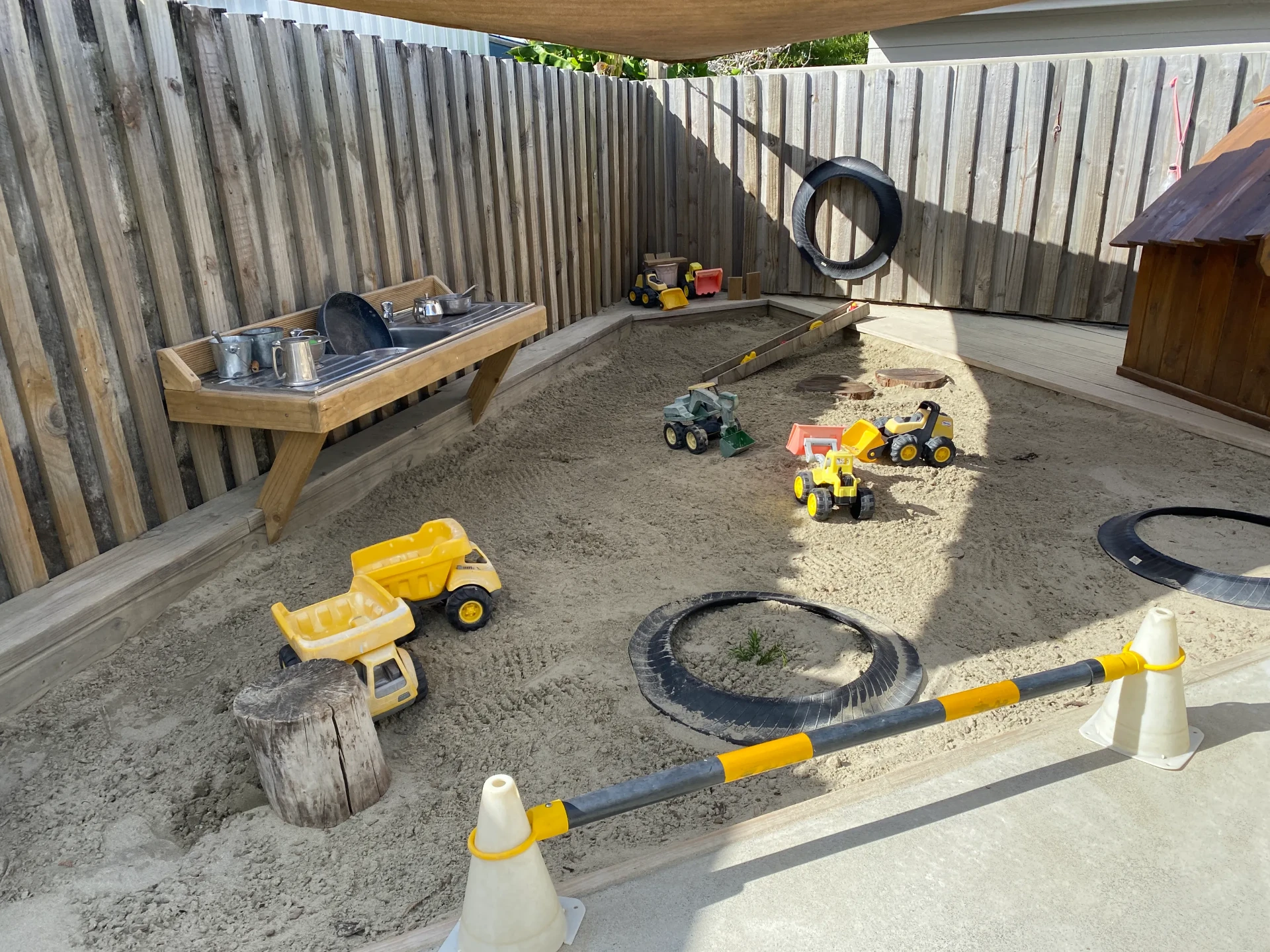 The shaded sandpit at Children's Ark with diggers, trucks and a timber mud kitchen bench