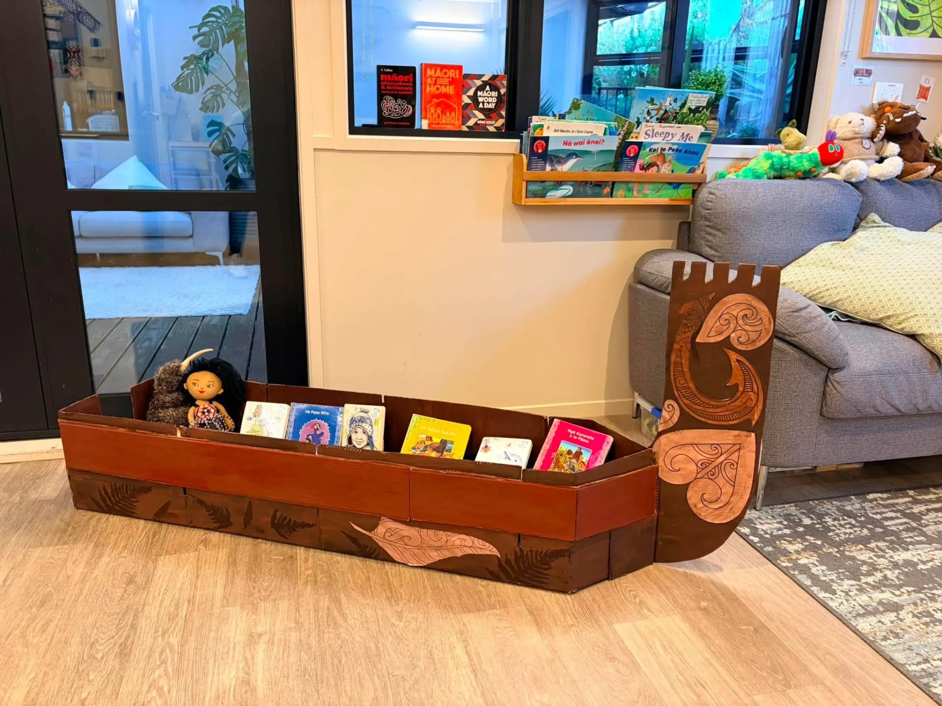 A carved waka book boat holding te reo Māori picture books in the Bee Room