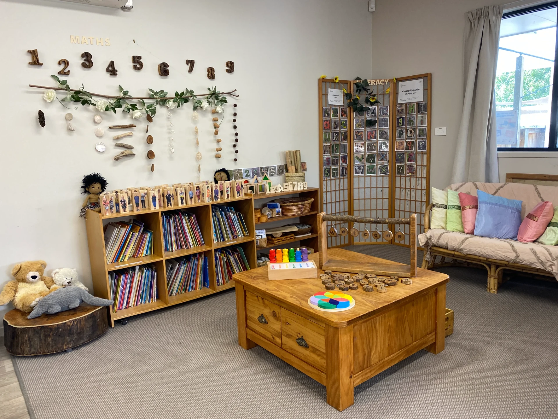 Maths and literacy corner in the Kākāpō Room with wooden numbers, natural materials, books and a cosy couch