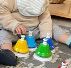 A baby playing with coloured musical hand bells on the floor