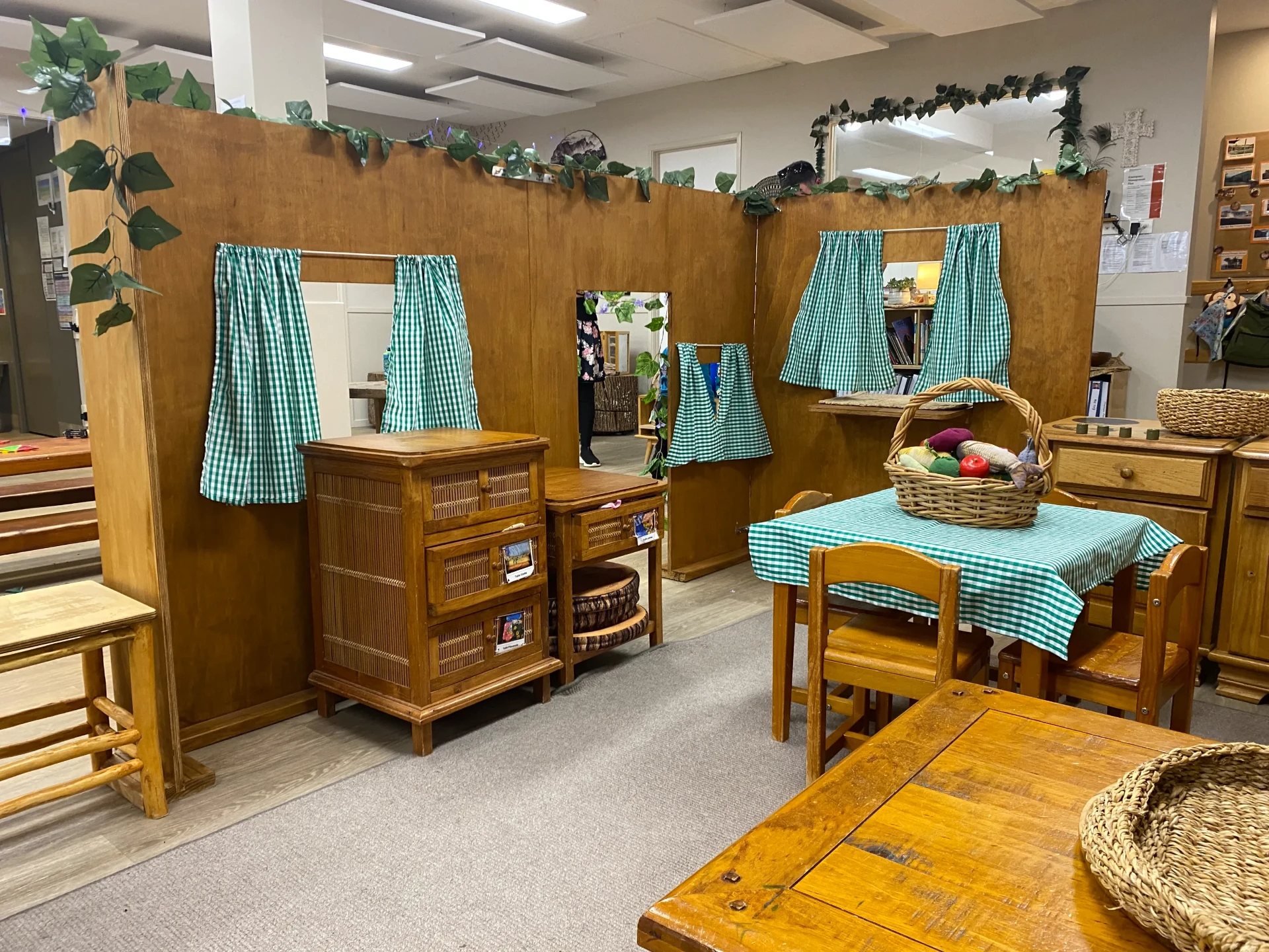 The Kākāpō Room home corner with a timber playhouse, gingham curtains and a set table