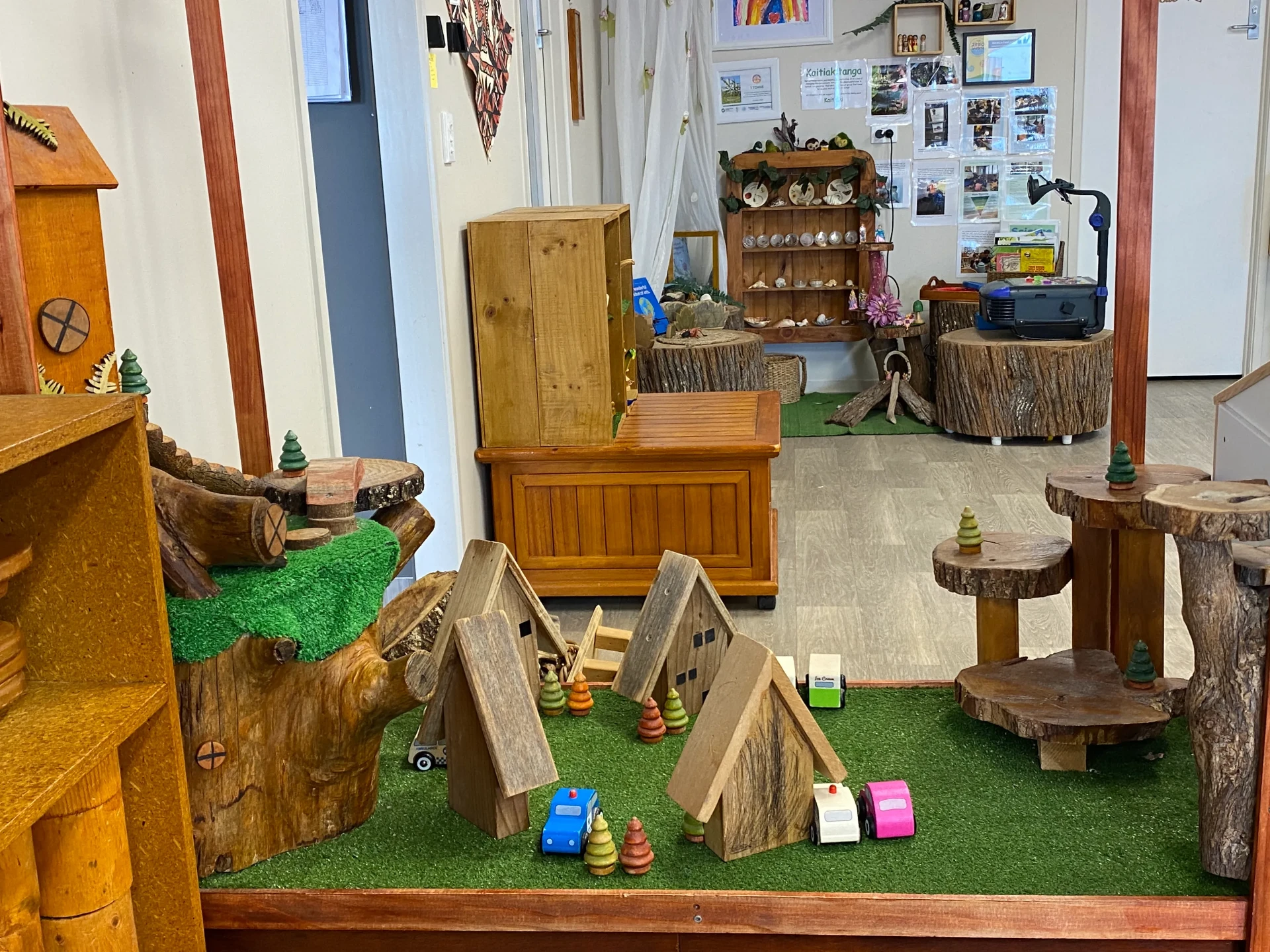 Indoor wooden tree village play area with timber huts, tree stump tables and a nature discovery shelf